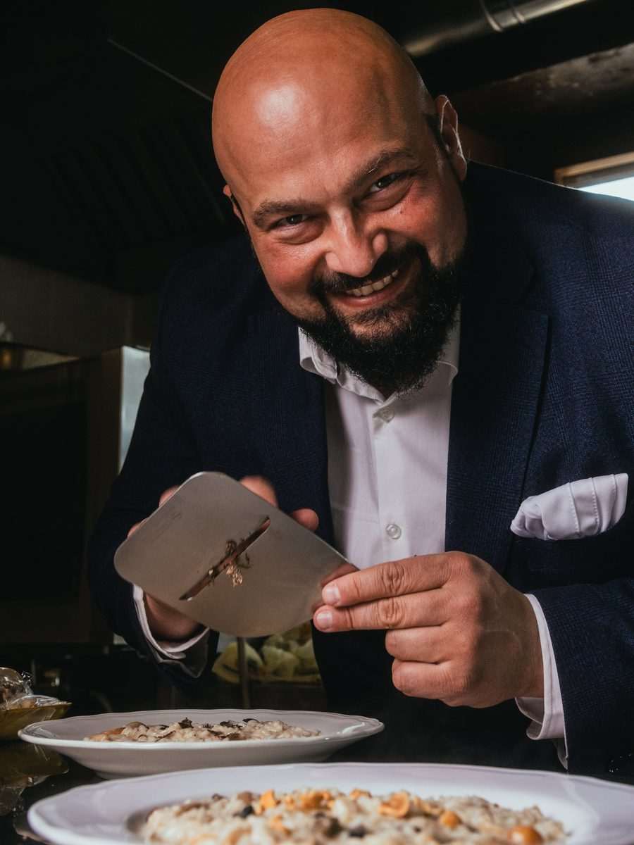Daniele Violoni in cucina, con l'affetta-tartufo sopra due piatti di risotto
